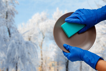 Women's hands in protective gloves with sponge and plate with winter on background.
