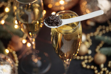Black caviar in a mother-of-pearl spoon and glass of champagne with Christmas holiday decoration, gold bokeh for New Year Eve party celebration, expensive delicious appetizer sea food - obrazy, fototapety, plakaty