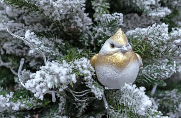 Ceramic figurine of a bird with a golden crest on the snow-covered Christmas tree.