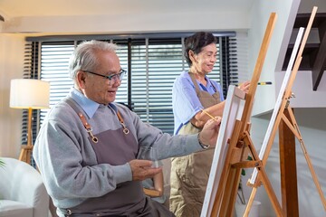 Couple Senior drawing at art. Side view portrait of white haired senior woman holding palette painting pictures at easel in art studio.
