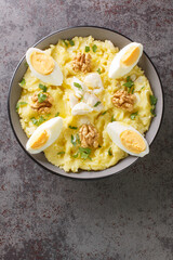 Spanish cuisine mashed potatoes with cod and garlic served with walnuts and boiled eggs close-up in a bowl on the table. Vertical top view from above