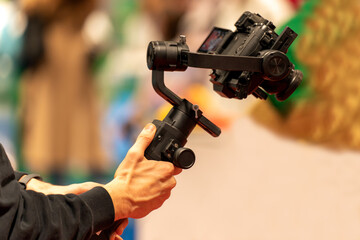 Unrecognizable man carrying stabilizer with modern camera while shooting video during public event