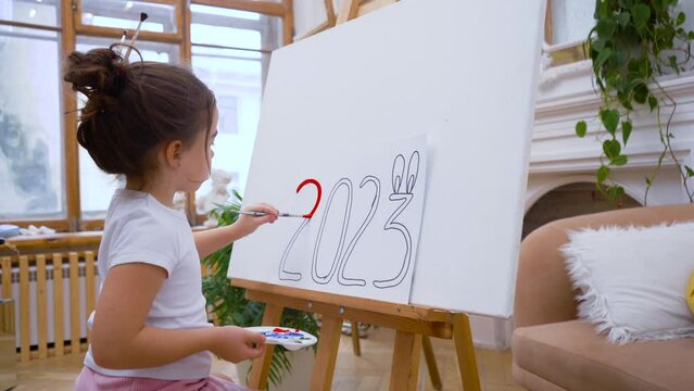 Girl draws the numbers 2023 on an easel. Happy New Year concept. Painting artist