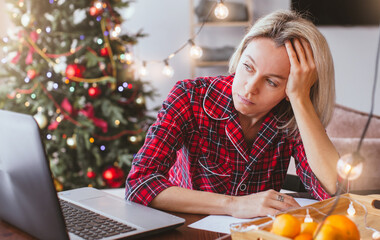 Sad middle aged woman working at the home office by laptop during Christmas holiday