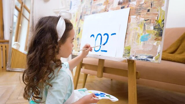 A girl painting on drawing easel with canvas palette and brush the numbers 2023 