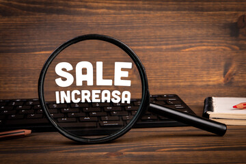 SALE INCREASA. Magnifying glass and computer on wooden office table