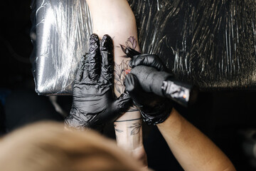 Top view of tattoo master making black tattoo with paint. Master works in black sterile gloves....