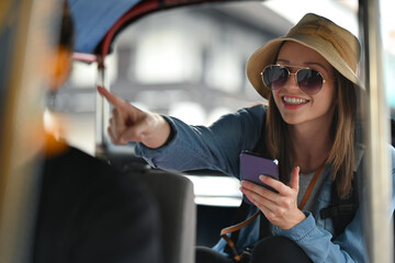 Smiling woman traveler using smartphone for helping tourism about travel map while sitting in tuk tuk public transport in Thailand