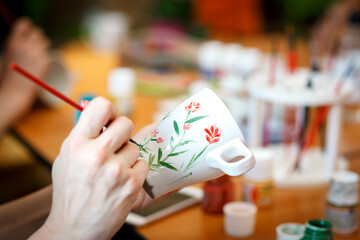 The girl paints a white cup.