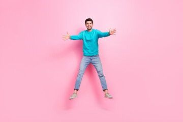 Fototapeta na wymiar Full length photo of attractive young man jumping stretching hands hug excited dressed stylish blue look isolated on pink color background