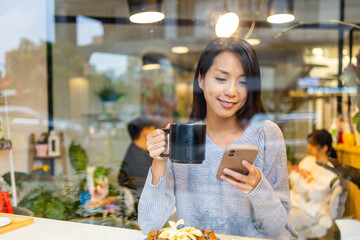 Woman use mobile phone and sit inside the coffee shop with window reflection