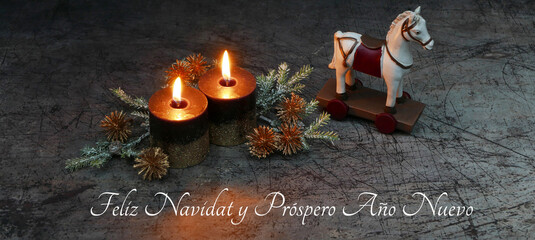 Tarjeta navideña: dos velas encendidas con ramas de abeto y caballo mecedor sobre madera vieja y...