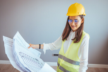 Portrait of woman engineer at building site looking at camera with copy space. Mature construction manager standing in yellow safety vest and blue hardhat with crossed arms. 