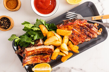 top view of a dark rectangular ceramic plate with grilled pork ribs and potato slices with parsley and spices. the concept of serving food.