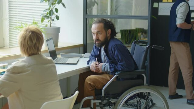 Businessman in wheelchair discussing job with female colleague while working together in office