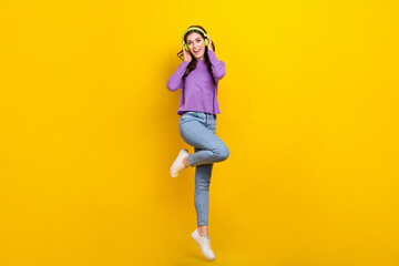 Fototapeta na wymiar Full size photo of cheerful pretty girl hands touch headphones jumping isolated on yellow color background