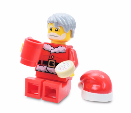 Lego minifigure of Santa Claus is  drinking milk and eating a cookie isolated on white. Editorial illustrative image of popular plastic toy constructor.