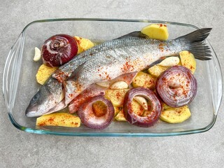 Raw sea bass fish prepared with with potatoes and onions to cook