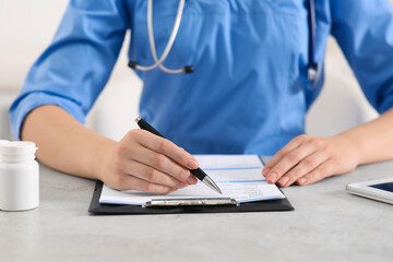 Doctor filling patient's medical card at table in clinic, closeup