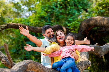 Happy indian couple sitting with his little girl on tree branch at garden.