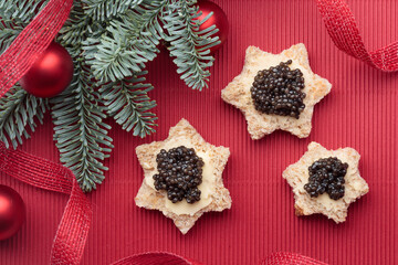 Black caviar appetizers bread stars on a christmas decorated red background