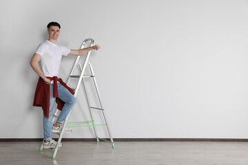 Handyman climbing up stepladder near white wall indoors. Space for text
