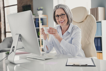 Obraz na płótnie Canvas Photo of pretty smiling lady trader dressed white shirt eyewear drinking hot tea relaxing indoors workstation workshop
