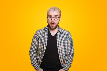 Portrait of a shocked bearded man in eyeglasses looking at camera isolated over yellow background. Stunned facial expression.