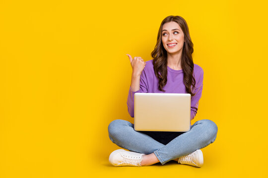 Full size photo of pretty girl sit floor look indicate finger empty space proposition isolated on yellow color background