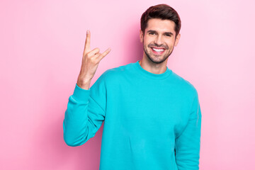 Photo of young positive cheerful handsome guy smiling enjoy his rock roll music album showing horned symbol fingers isolated on pink color background