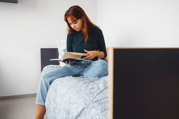 Young woman studying music reading a book on her bed in the dorm room