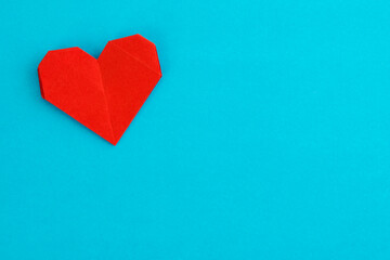 Red origami heart on blue background