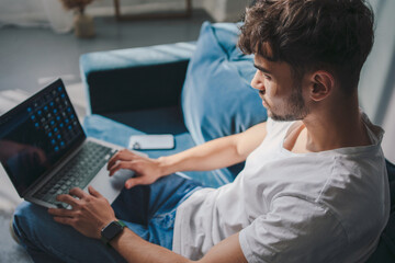 Serious caucasian man using laptop computer watching videos during free time at home interior. Shop on internet. Choose product to order online. Watch streaming