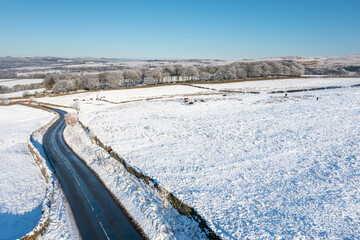 Aerial drone photo of the town of Mereclough in the town of Burnley in Lancashire, England showing the farmers fields on a snowy winters day in the UK with snow covering the fields and a blue sky.