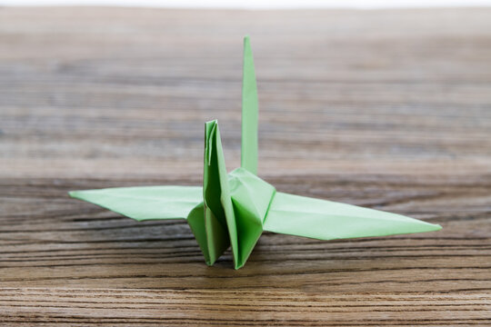 Green origami paper crane on wooden table