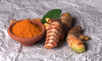 Turmeric powder in wooden bowl and fresh turmeric root on textured background. Herbs are native ,Food and drink, diet nutrition, health care concept.