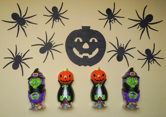 Cute characters in monster costume. Scary Halloween figurines stand on a light background close-up, behind hangs terrible black pumpkin. Halloween concept. Holiday decorations