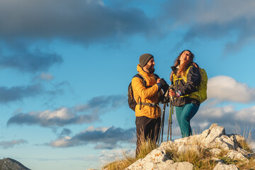 couple of hikers with backpacks and trekking poles contemplating the landscape after having reached the summit of a mountain peak. man and woman hiking. outdoor sport. - obrazy, fototapety, plakaty