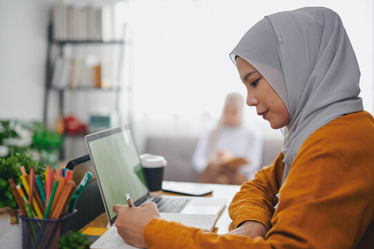 Islamic woman wearing hijab headscarf studying online with laptop.