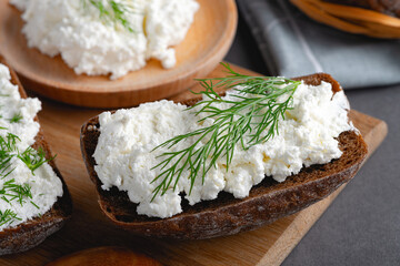 Home made rye bread on a wooden cutting board with curd cheese, ricotta and dill