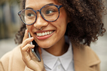 Close up of afro american woman wearing glasses talking phone with friends during city walking