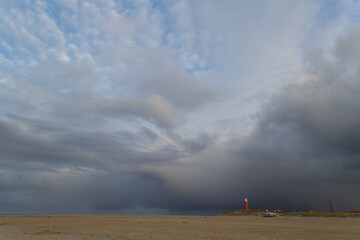 Fototapeta na wymiar Rain clouds menacingly approach the lighthouse on the Dutch island Texel in the Wadden sea over the wide beach