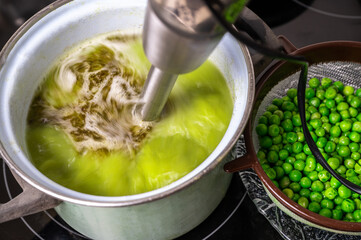 Stick blender blends pea soup in pot on hob, raw pea. - 553713613