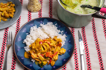 Homemade dining, luch or dinner. Asian food (turkey meat with vegetable and rice) on blue plate, pea soup in pot on table.