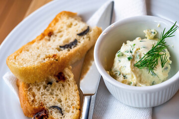 Italian bread with dried tomato and olive, chive butter with dill in bowl.