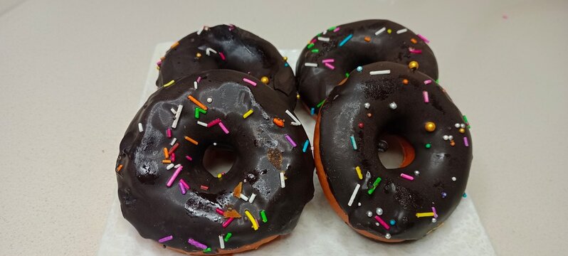 assorted donuts with chocolate frosted, pink glazed and sprinkles donuts. Donuts in hand or tray
