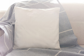 Square white pillow on the sofa in bright sunlight. Mockup for design.
