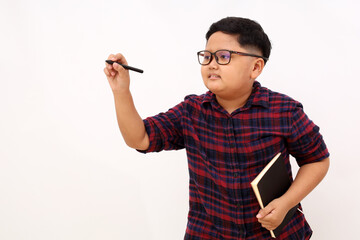 Happy Asian school boy standing while writing something and carrying a book. Isolated on white background