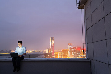 Businessman sitting on the rooftop and using laptop