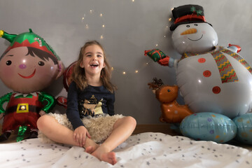 Cute little girl sitting on the play mat with funny expression. Christmas balloon and lights...
